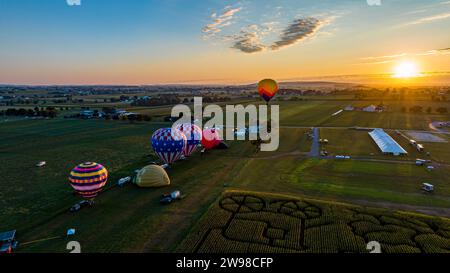 Eine lebendige, farbenfrohe Landschaft mit mehreren Heißluftballons, die im Himmel schweben, während die Sonne im Hintergrund untergeht Stockfoto