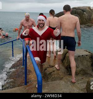 Schwimmer, die als weihnachtsmann gekleidet sind und am jährlichen Weihnachtstag teilnehmen, schwimmen am vierzig Fuß langen Badeplatz in Sandycove Dublin. Bilddatum: Mittwoch, 13. Dezember 2023. Stockfoto