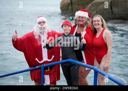 Patrick Corkery als Weihnachtsmann gekleidet und sein Sohn Matthew, 12 Jahre alt, als Elf gekleidet, posieren für ein Foto mit anderen Schwimmern, nachdem sie am 1. Weihnachtsfeiertag am vierzig Fuß Badeplatz in Sandycove Dublin teilgenommen haben. Bilddatum: Mittwoch, 13. Dezember 2023. Stockfoto