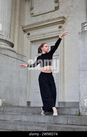 Eine junge Frau in schwarzem Outfit, die einen zeitgenössischen Tanz auf Steintreppen vorführt Stockfoto