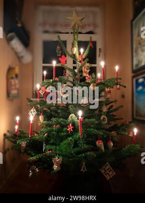 Weimar, Deutschland. Dezember 2023. In der Ecke eines Wohnzimmers steht am Heiligabend ein Weihnachtsbaum, dekoriert mit beleuchteten Kerzen und kleinen Figuren. Quelle: Soeren Stache/dpa/Alamy Live News Stockfoto