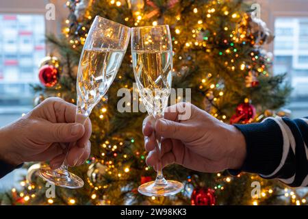 Silvester- oder weihnachtsessen, zwei Mannhände mit Gläsern Sekt Cava oder Prosecco in Kristallgläsern mit weihnachtsbaum- und Girlandenbeleuchtung Stockfoto