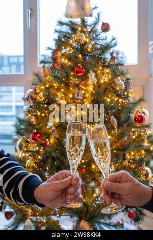 Silvester- oder weihnachtsessen, zwei Mannhände mit Gläsern Sekt Cava oder Prosecco in Kristallgläsern mit weihnachtsbaum- und Girlandenbeleuchtung Stockfoto