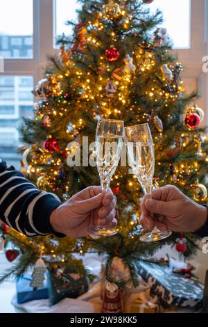 Silvester- oder weihnachtsessen, zwei Mannhände mit Gläsern Sekt Cava oder Prosecco in Kristallgläsern mit weihnachtsbaum- und Girlandenbeleuchtung Stockfoto