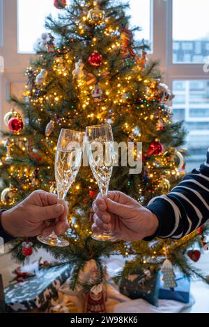 Silvester- oder weihnachtsessen, zwei Mannhände mit Gläsern Sekt Cava oder Prosecco in Kristallgläsern mit weihnachtsbaum- und Girlandenbeleuchtung Stockfoto