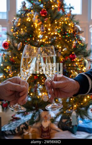 Silvester- oder weihnachtsessen, zwei Mannhände mit Gläsern Sekt Cava oder Prosecco in Kristallgläsern mit weihnachtsbaum- und Girlandenbeleuchtung Stockfoto