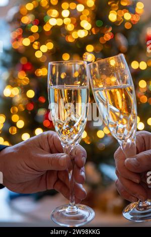 Silvester- oder weihnachtsessen, zwei Mannhände mit Gläsern Sekt Cava oder Prosecco in Kristallgläsern mit weihnachtsbaum- und Girlandenbeleuchtung Stockfoto