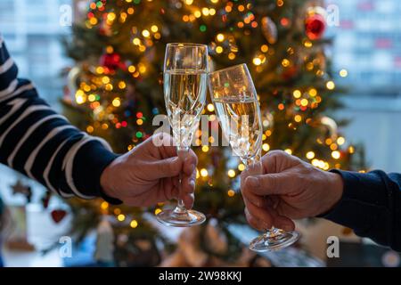 Silvester- oder weihnachtsessen, zwei Mannhände mit Gläsern Sekt Cava oder Prosecco in Kristallgläsern mit weihnachtsbaum- und Girlandenbeleuchtung Stockfoto
