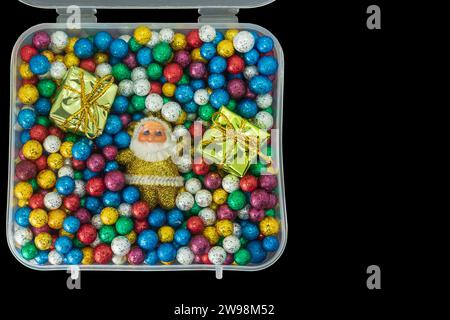 Weihnachtsmann mit einem Stapel von kleinen bunten Thermokolkugeln und Geschenkbox in Plastikbox isoliert auf schwarzem Hintergrund. Draufsicht Stockfoto
