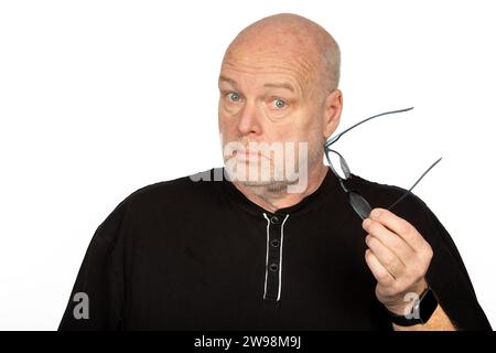 Überraschter kaukasischer Mann mittleren Alters, der einen dunklen Brillenrahmen auf weißem Hintergrund hält - schockierter Ausdruck - Kopf leicht gedreht Stockfoto