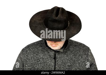 Ernster kaukasischer Mann mittleren Alters in schmutzigem schwarzen Cowboyhut, der auf weißem Hintergrund nach unten blickt Stockfoto