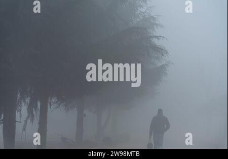 Srinagar, Indien. Dezember 2023. Ein Mann läuft bei dichtem Nebel auf einer Straße in Srinagar. Intensive Kälte gepaart mit dichtem Nebel und Dunst störte das normale Leben im Kaschmir-Tal am Montag. Srinagar und andere Teile des Kaschmir-Tals waren von einer dicken Schicht Nebel und Dunst umgeben, die die Sicht einschränkte und Pendlern Unannehmlichkeiten bereitete. (Foto: Idrees Abbas/SOPA Images/SIPA USA) Credit: SIPA USA/Alamy Live News Stockfoto