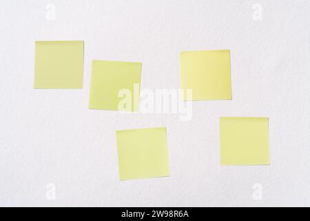 Fünf leere gelbe Post-it-Notizen (Haftnotizen) auf weißem Papierhintergrund. Abstrakter Hintergrund mit Kopierraum für Text oder Nachricht. Stockfoto