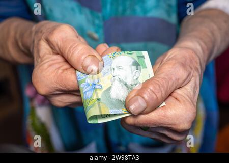 Eine alte rumänische Frau klammert eine 1-Leu-Banknote in ihren verschlissenen Händen, Finanzkonzept, rumänisches Geld, Probleme von älteren und armen Menschen Stockfoto