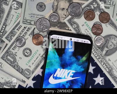 Deutschland. Dezember 2023. In dieser Fotoabbildung ist ein Nike Unternehmenslogo auf einem Smartphone mit US-Dollar-Banknoten und -Münzen im Hintergrund zu sehen. (Foto von Igor Golovniov/SOPA Images/SIPA USA) *** ausschließlich für redaktionelle Nachrichten *** Credit: SIPA USA/Alamy Live News Stockfoto