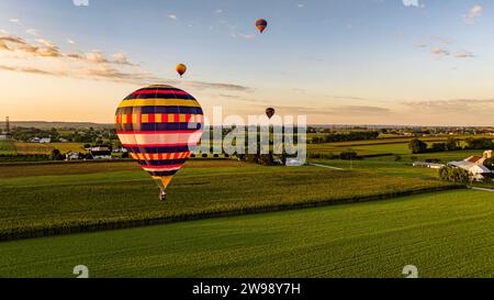 Ein Blick aus der Vogelperspektive auf vier Heißluftballons, die an einem sonnigen Sommertag über ländliches Ackerland von Maisfeldern und Alfalfa schweben Stockfoto