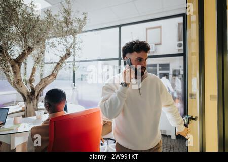 Gutaussehender Mann, der während eines Telefonanrufs aus dem Büro geht. Stockfoto