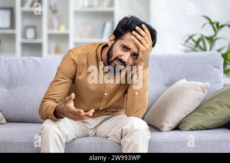 Porträt eines jungen Indianers, der verärgert in die Kamera schaut, seine Hände frustriert ausbreitet, an Kopfschmerzen und Depressionen leidet. Stockfoto