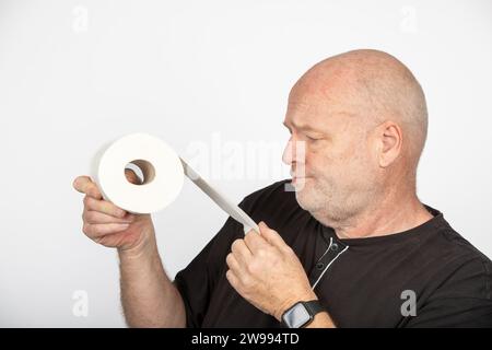 Skurriler Wahnsinn: Mann mittleren Alters, der Toilettenpapierrolle auf weißem Hintergrund hält Stockfoto