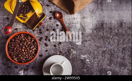 Schüssel mit Kaffeebohnen neben einer leeren Tasse und einem Mahlwerk mit gemahlenem Kaffee auf einem grauen Marmortisch. Stockfoto