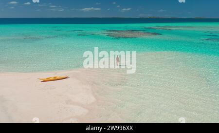 Tropischer Inselstrand mit Korallenriff kristallklarem türkisfarbenem Wasser. Frau zurück Blick im Meer stehend genießen Sie wunderschöne wilde Naturlandschaft. Gelbes Kajak. Sommerferien. Drohnenaufnahme Stockfoto