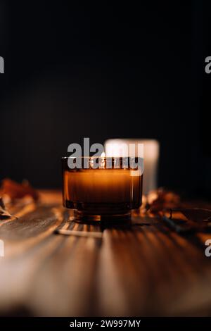 Eine orangene Kerze in einem Keramikbecher auf einem Holztisch in einer isolierten Umgebung Stockfoto