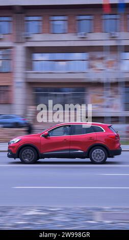 Ein modernes rotes Auto parkt mitten in einer belebten Straße, ein weiteres Auto fährt im Hintergrund vorbei Stockfoto