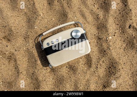 Ein klassisches Radio an einem Sandstrand, umgeben von Felsen, mit einem ruhigen Meer im Hintergrund Stockfoto