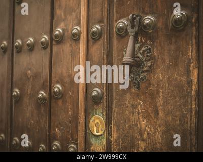Eine alte, abgenutzte Holztür mit Metallnieten und schwarzem Klopfer in Sevilla, Andalusien, Spanien Stockfoto