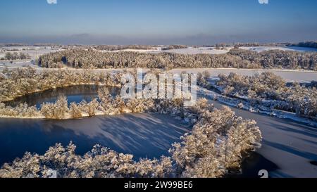 Ein Blick aus der Vogelperspektive auf schneebedeckte Bäume, die einen Fluss inmitten eines Waldes umgeben. Stockfoto