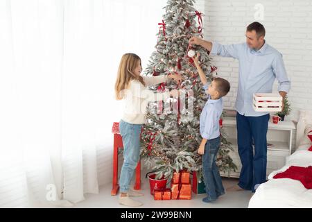 Vater, Tochter und Sohn spielen in einem schönen hellen Raum in der Nähe eines wunderschön dekorierten Weihnachtsbaumes. Stockfoto