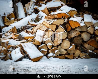 Ein mit Schnee bedeckter Holzhaufen befindet sich im Winter auf dem Boden Stockfoto