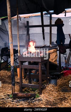 Ein Lagerfeuer, das hell brennt, mit Funken, die sich vor dem Hintergrund eines Zeltbereichs erheben, umgeben von Heuballen Stockfoto