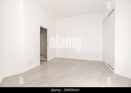 Ein Zimmer mit unregelmäßigen Wänden und eingebautem Kleiderschrank mit weißen Schiebetüren, hellen Holzböden und weißen Wänden Stockfoto