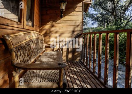 Eine Holz- und Korbbank auf der Veranda einer Blockhütte mit einem Holzgeländer Stockfoto