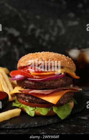 Köstlicher Burger mit Fleischkoteletts, Speck, Käse, Gemüse und Salat auf schwarzem Tisch Stockfoto