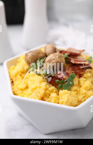 Gekochtes Maismehl mit Speck, Pilzen und Mikrogrün in Schüssel auf weißem Marmortisch, Nahaufnahme Stockfoto