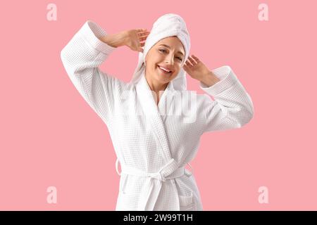 Reife Frau im Bademantel nach der Dusche auf rosa Hintergrund Stockfoto