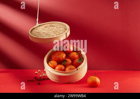 Mandarinen werden in einem Bambusdampfer auf rotem Hintergrund gelagert. Mandarinen sollen Anfang des Jahres Glück bringen. Tet-Thema. Stockfoto