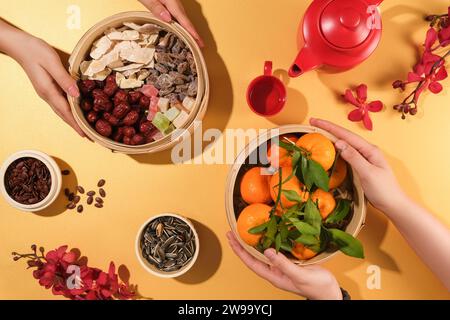 Mandarinen, Jujubes, gesalzene getrocknete Früchte, Gummibonbons und Marmelade werden in Bambusdampfern gelagert, Melonen- und Sonnenblumenkerne in kleinen Schüsseln, einem Teeset und Re Stockfoto