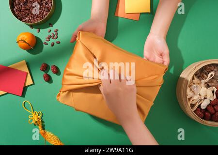 Tet-Geschenk-Szene. Geschenkbox in der Mitte des Rahmens, Melonensamen-Tablett, Marmelade-Tablett und Glücksgeld-Umschlag auf grünem Hintergrund mit Draufsicht. Stockfoto