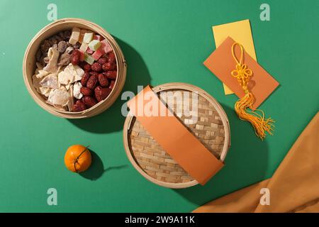 Marmelade, gesalzene getrocknete Früchte, Jujube und Gummibonbons befinden sich in einem Bambusdampfer, Mandarinen- und roten Umschlägen auf grünem Hintergrund. Tet-Szene für Adver Stockfoto