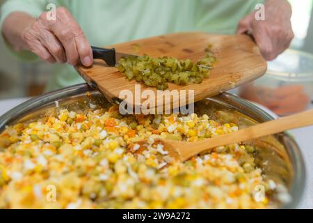 Eine ältere Dame macht einen Gemüsesalat. Schneiden einer eingelegten Gurke für eine gesunde Mahlzeit auf einem Schneidebrett. Stockfoto