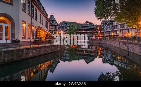 Verzierte traditionelle Fachwerkhäuser mit blühenden Blumen entlang der Kanäle im Viertel Petite France in Straßburg, Elsass, Frankreich bei Sonnenuntergang Stockfoto