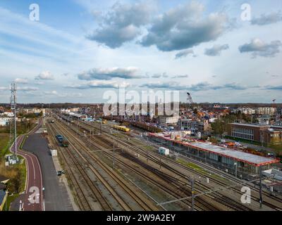 Das Bild bietet eine umfassende Tagesansicht des Bahnhofs Lier in Belgien und fängt das Wesen des täglichen Lebens und des Verkehrs ein. Züge werden geparkt und in Bewegung gesehen, was die Funktion des Bahnhofs als Verkehrsknotenpunkt verdeutlicht. Die umliegende städtische Landschaft ist mit architektonischen Details gespickt, von Wohngebäuden bis hin zur historischen Stadtkulisse. Die Bautätigkeit in der Nähe des Bahnhofs weist auf Wachstum und Entwicklung hin, während der wolkenreiche Himmel darüber der Szene ein dynamisches Element verleiht. Bahnhof Lier bei hellerem Tageslicht. Hochwertige Fotos Stockfoto