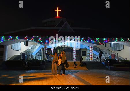 Mumbai, Indien. Dezember 2023. Die Leute machen ein Selfie vor einer Kirche, die mit Lichtern beleuchtet ist, um das Weihnachtsfest in Mumbai zu feiern. Weihnachten wird in aller Welt gefeiert, um an die Geburt Jesu Christi zu erinnern. Menschen aus der christlichen Gemeinde schmücken ihr Haus mit Weihnachtsbaum und Lichtern, tauschen Geschenke aus und Familienmitglieder versammeln sich zu einem fest, um den Anlass zusammen mit ihren nahen und lieben Menschen zu feiern. Quelle: SOPA Images Limited/Alamy Live News Stockfoto