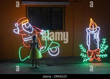 Mumbai, Indien. Dezember 2023. Ein Mädchen posiert für ein Foto in der Nähe der Lichtinstallation des Weihnachtsmanns, der auf einem Motorrad fährt, das auf der Straße gehalten wird, um das Weihnachtsfest in Mumbai zu feiern. Weihnachten wird in aller Welt gefeiert, um an die Geburt Jesu Christi zu erinnern. Menschen aus der christlichen Gemeinde schmücken ihr Haus mit Weihnachtsbaum und Lichtern, tauschen Geschenke aus und Familienmitglieder versammeln sich zu einem fest, um den Anlass zusammen mit ihren nahen und lieben Menschen zu feiern. Quelle: SOPA Images Limited/Alamy Live News Stockfoto