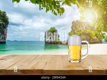 Das Bier wird auf einem Holztisch platziert und bietet Blick auf den tropischen, verschwommenen Strand. Zur Produktanzeige. - Strand- und Sommerkonzepte. Stockfoto