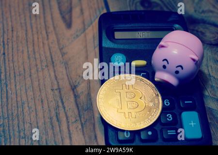 Taschenrechner mit dem Text „NFT“ mit einer Schweinebank und einem Bitcoin auf der Oberseite. Konzept der Investition der Ersparnisse in Kryptowährung . Stockfoto