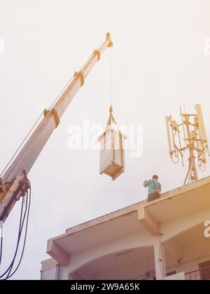 Industriekrane zum Betrieb und Anheben der elektrischen Box gegen Wolken und Himmel mit Telekommunikationsturm Stockfoto